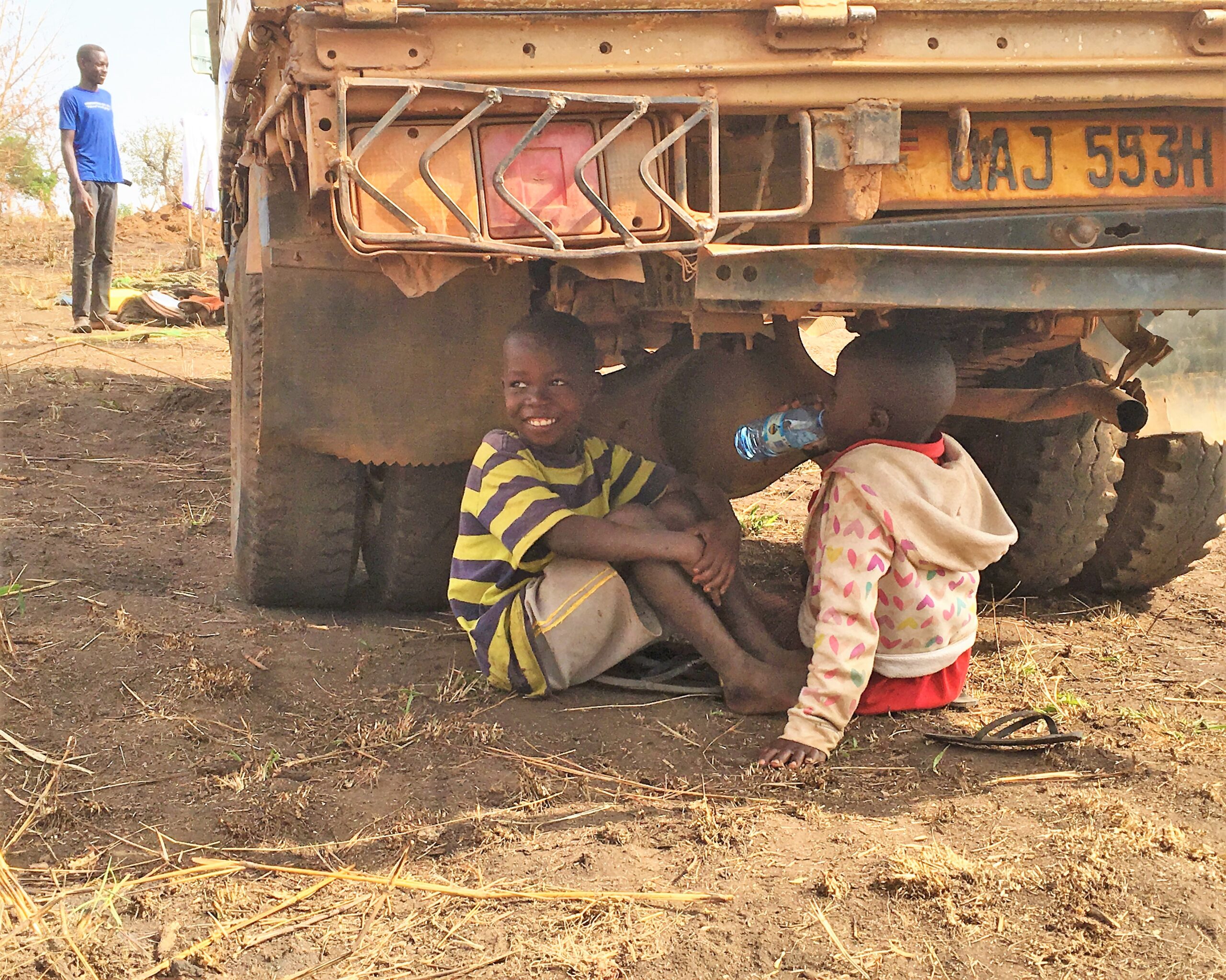 Boys sitting under the drilling truck with a cup of cold water